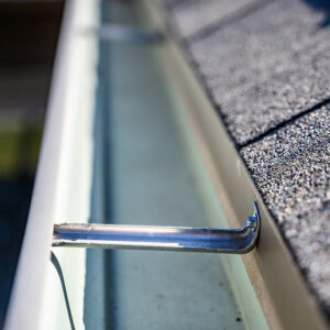 Close-up of a clean gutter attached to a shingled roof after thorough gutter cleaning service.